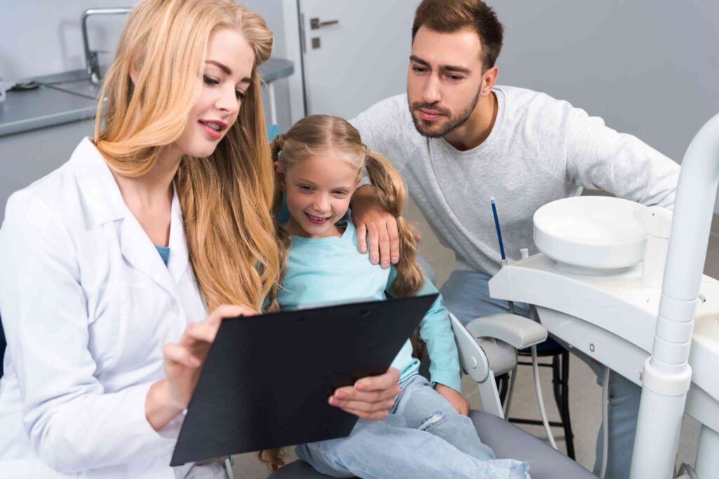 Child seated for an oral checkup while the father remains beside them.